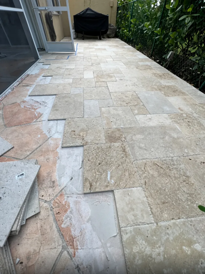 Travertine patio in French-pattern layout, mid-installation outside a screened lanai