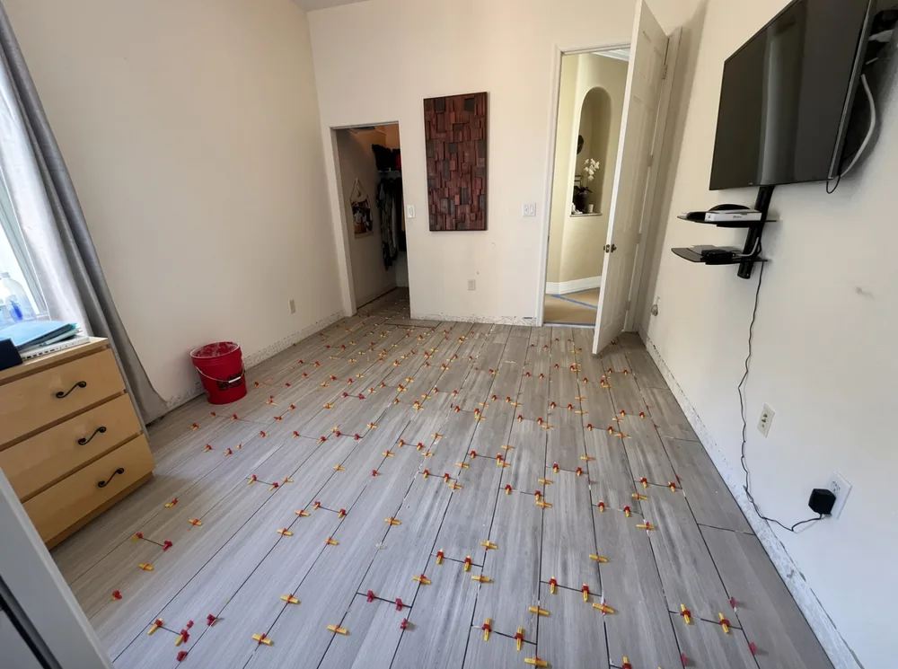 Wood-look porcelain plank tile mid-installation with leveling clips and wedges across the floor